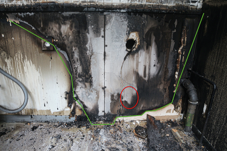 Bild 12 / Blick auf den Bereich mit den intensivsten und räumlich gesehen tiefsten Brandzehrungen im Bereich hinter der ehemaligen Aufstellposition eines Kühlschrankes: Diese beginnen bereits im bodennahen Bereich (grüne Markierung), weisen jedoch auf einer Höhe von etwa 20 cm über dem Bodenniveau noch eine weitere Freibrennung der Rußbeaufschlagungen auf (rote Markierung).