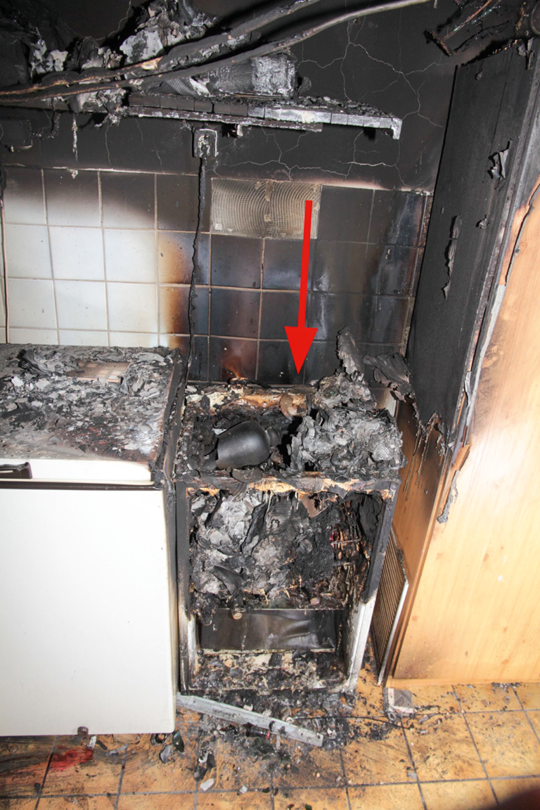 Bild 9 / Die Brandstelle im Keller mit  dem stark brandbetroffenen Kühlschrank (Pfeil
